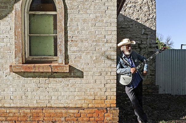 A photograph from the exhibition of a man leaning against a wall with his banjo